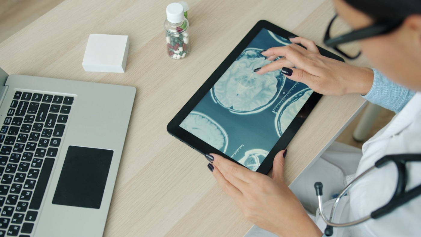 Clinician reviewing MRI scans on a tablet beside a laptop